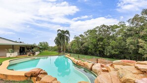 A swimming pool with a curved edge, surrounded by large rocks and a grassy area.