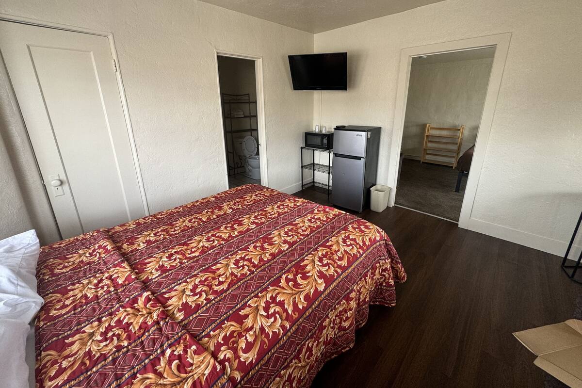 Un dormitorio con cama, televisión, refrigerador y una pequeña zona de kitchenette.