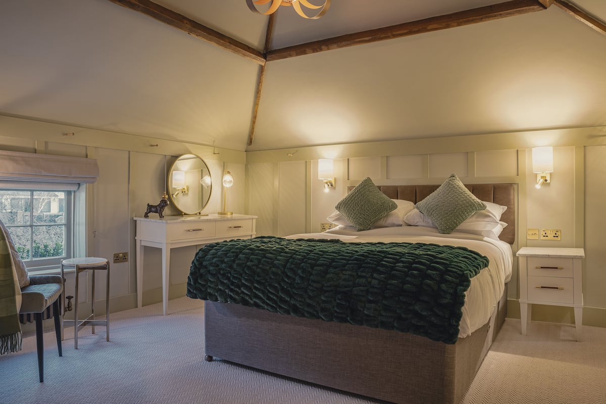 Ein Schlafzimmer mit einem großen Bett, Nachttischen, einem Schminktisch und einem Spiegel sowie einem Fenster.