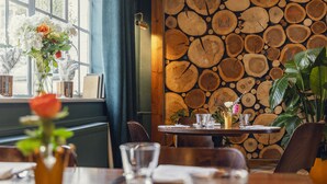 A dining area with a rustic wooden wall, a window with curtains, and a table set for two. - The Crown Inn at Burnham Beeches (Slough)
