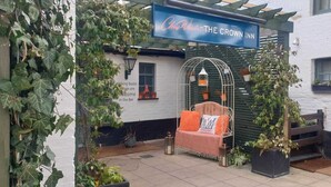 A cozy outdoor seating area with a bench and a hanging birdcage, surrounded by ivy and potted plants, in front of The Crown Inn. - The Crown Inn at Burnham Beeches (Slough)