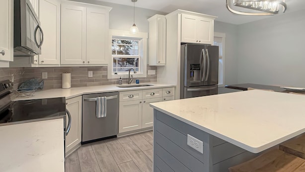 A modern kitchen with white cabinetry, a stainless steel refrigerator, a built-in oven, and a large island with a wooden stool.