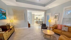 A spacious living area with a sofa, coffee table, and a TV. There is a kitchen in the background and a dining area.