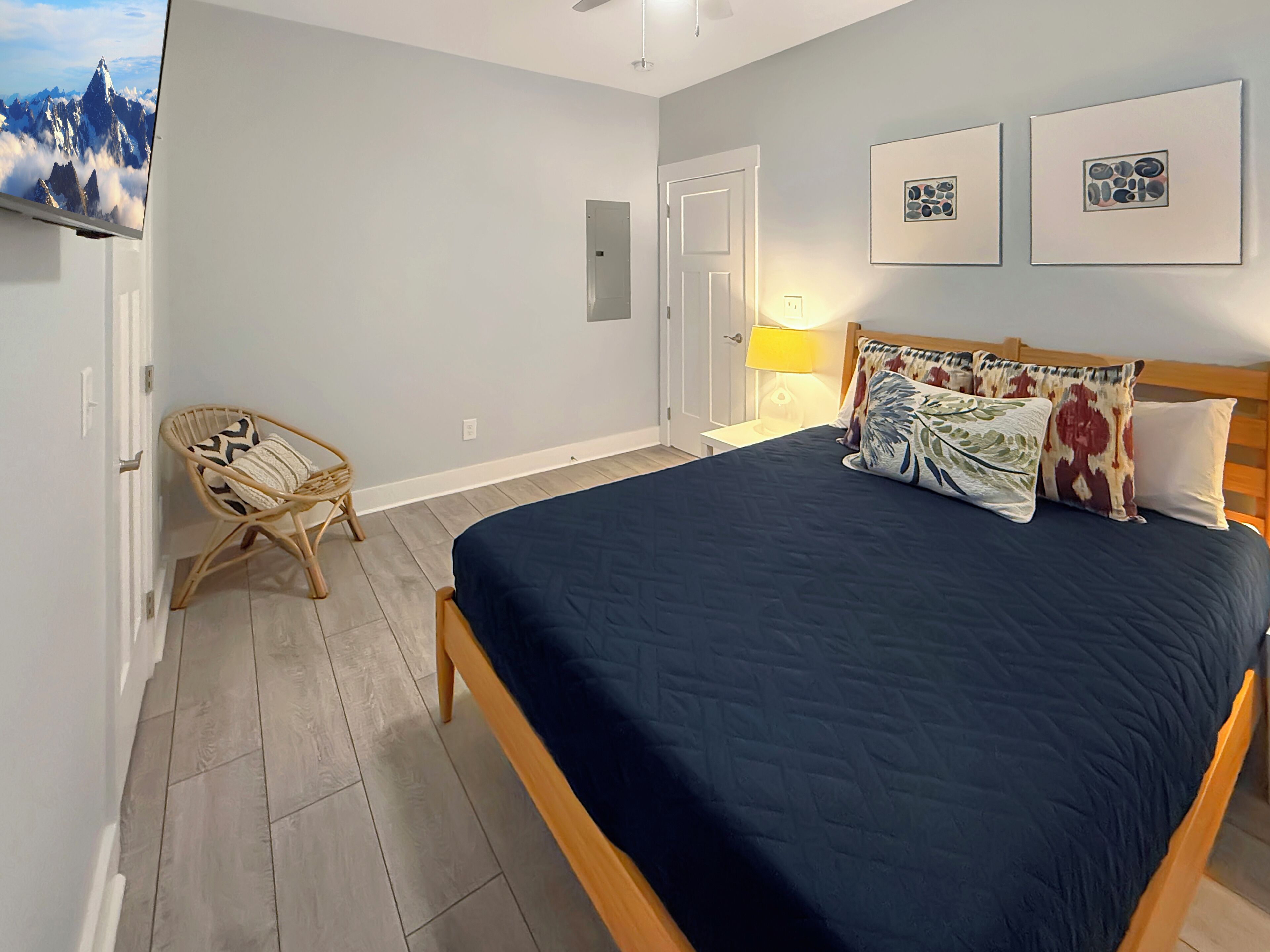 A bedroom with a bed, a chair, a wall-mounted TV, and framed artwork.