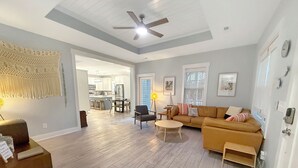 A spacious living room with a wooden floor, a sofa, a coffee table, and a dining area in the background.