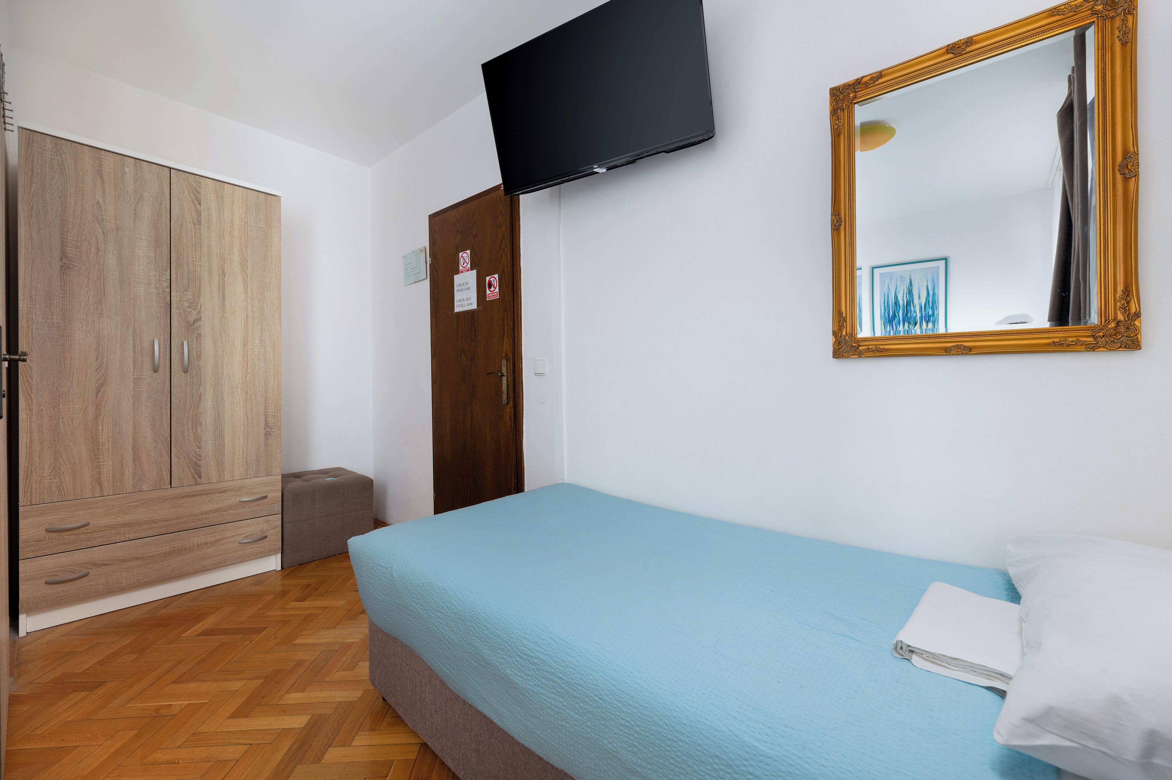 A bedroom with a bed, a wardrobe, a television, and a mirror.