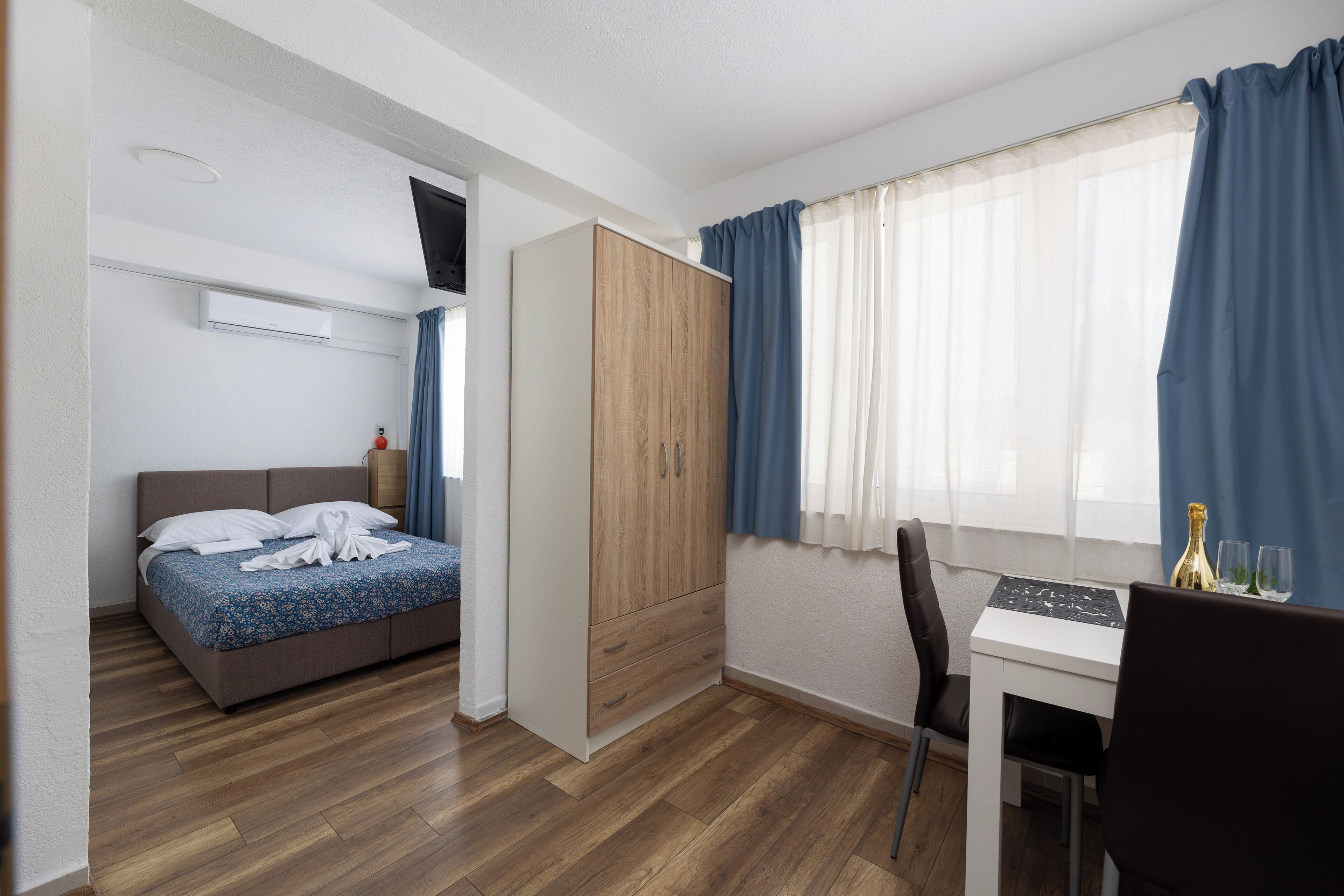 A hotel room with a bed, a wardrobe, a desk, and a window with curtains.