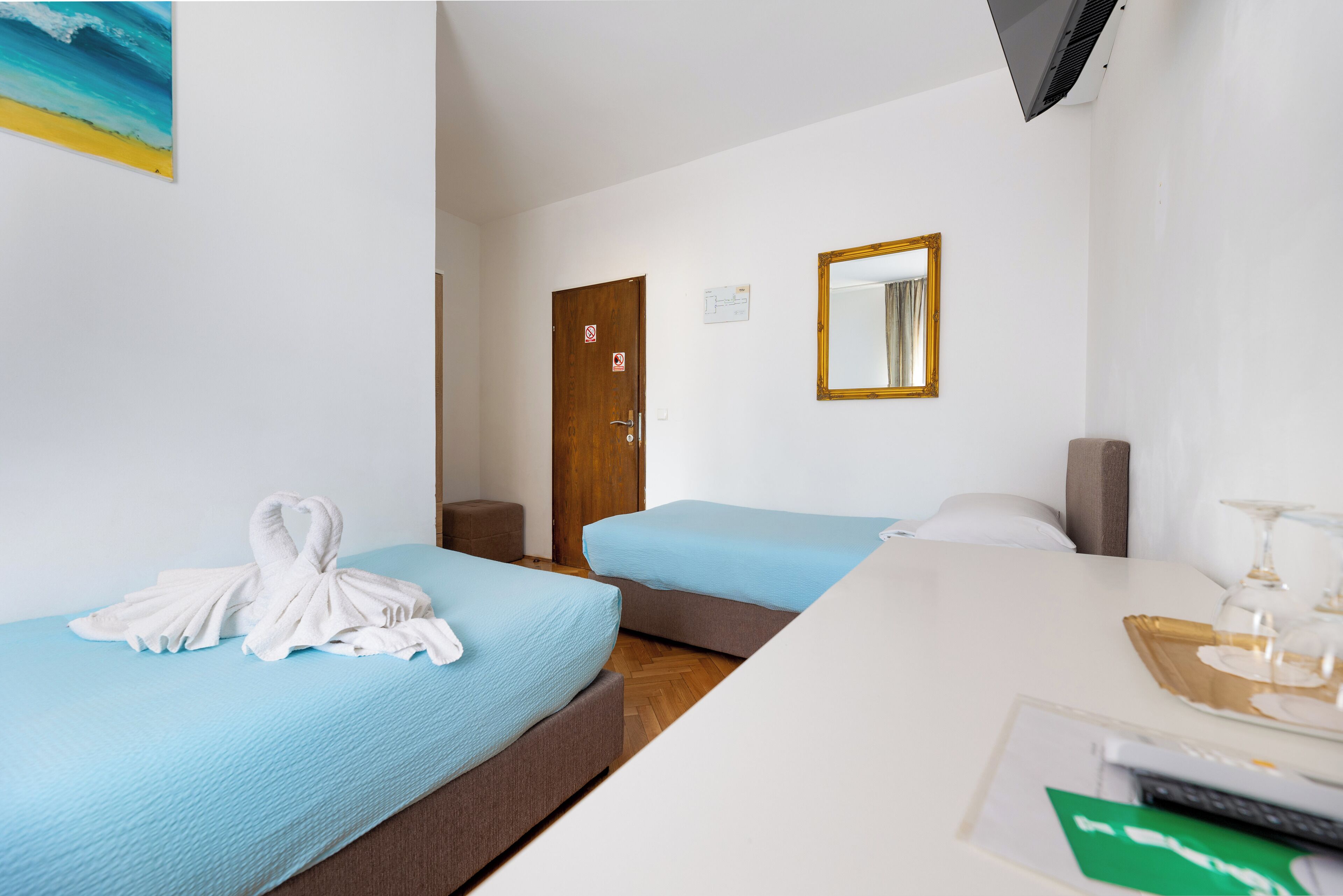 A hotel room with two beds, a desk with a glass, and a TV mounted on the wall.