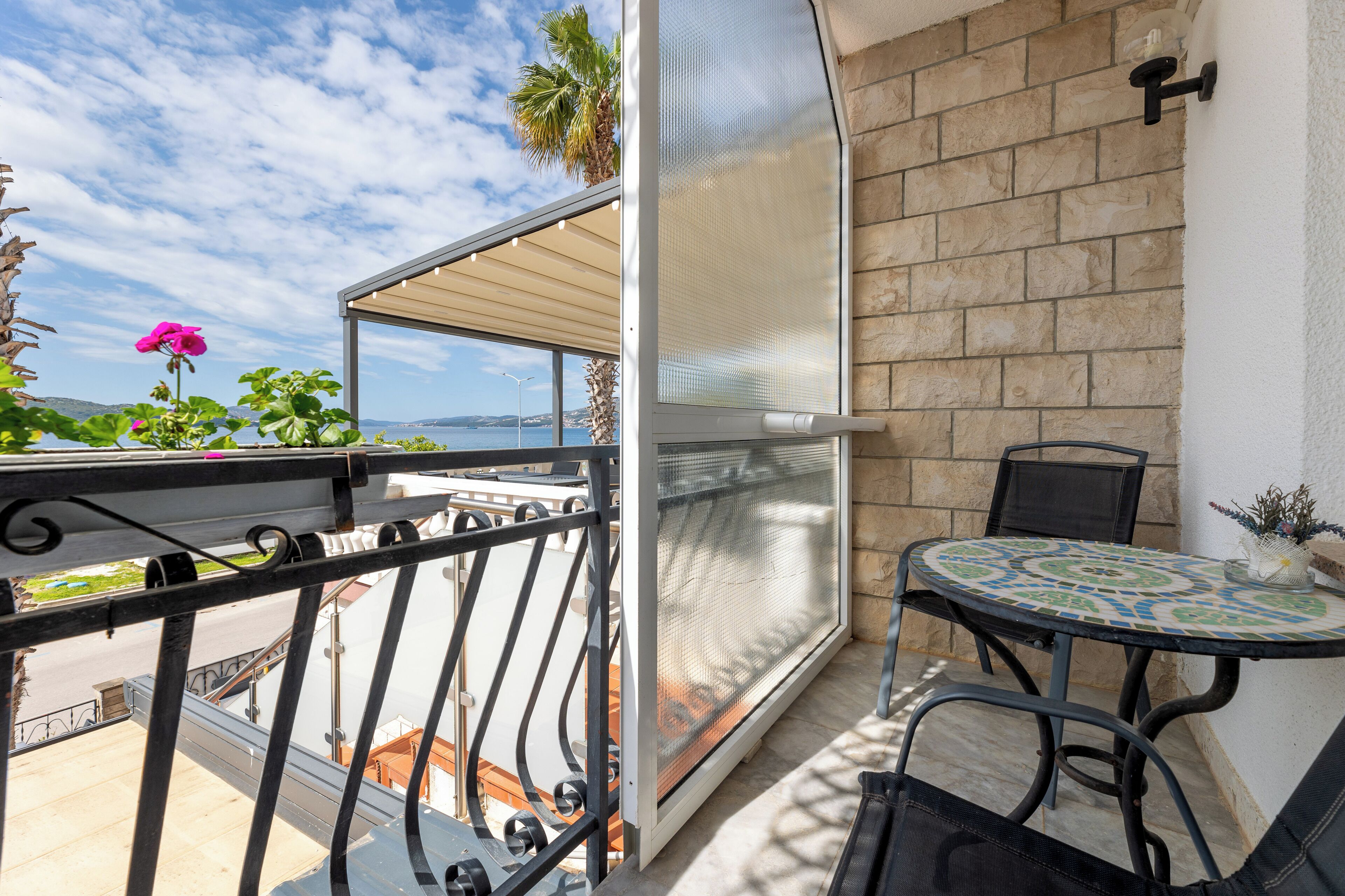 A balcony with a view of the sea, a table with chairs, and a potted plant.