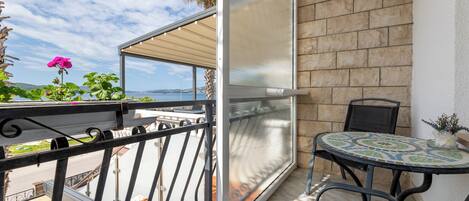 A balcony with a view of the sea, a table with chairs, and a potted plant.