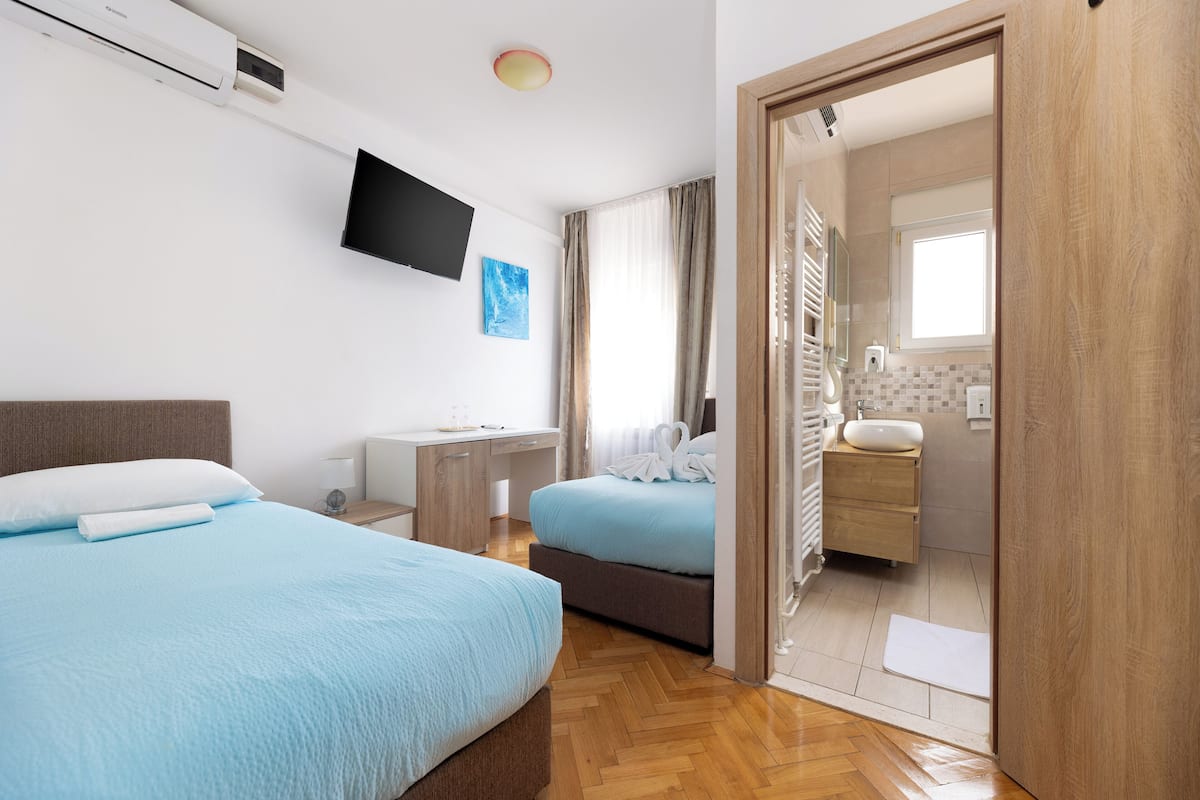 A hotel room with two beds, a desk, a flat-screen TV, and a bathroom visible through an open door.