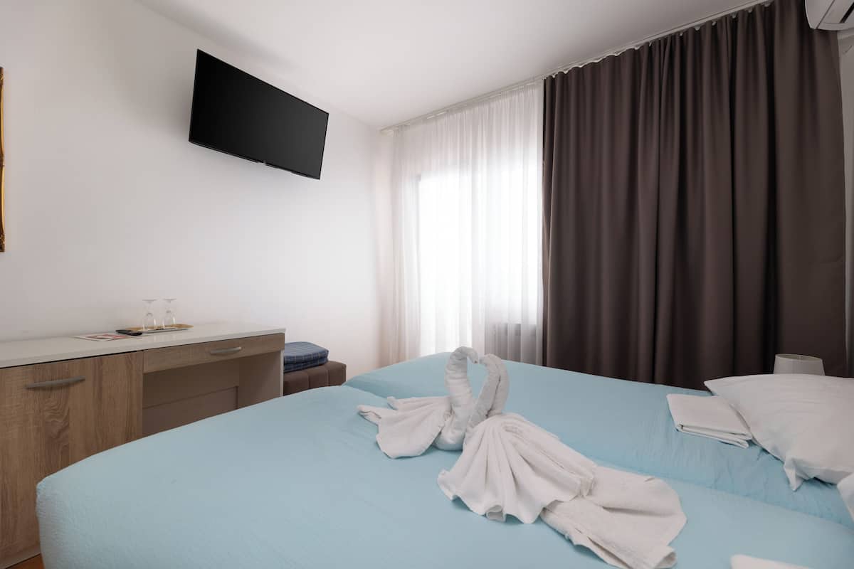 A hotel room with a bed, a desk, a flat-screen TV, and a window with curtains.