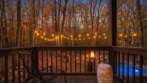 Um deck de madeira com uma cadeira e um abajur decorativo, com vista para uma floresta e área de piscina.