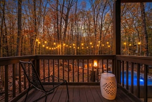 Une terrasse en bois avec une chaise et une lampe décorative, donnant sur une forêt et une zone avec piscine.