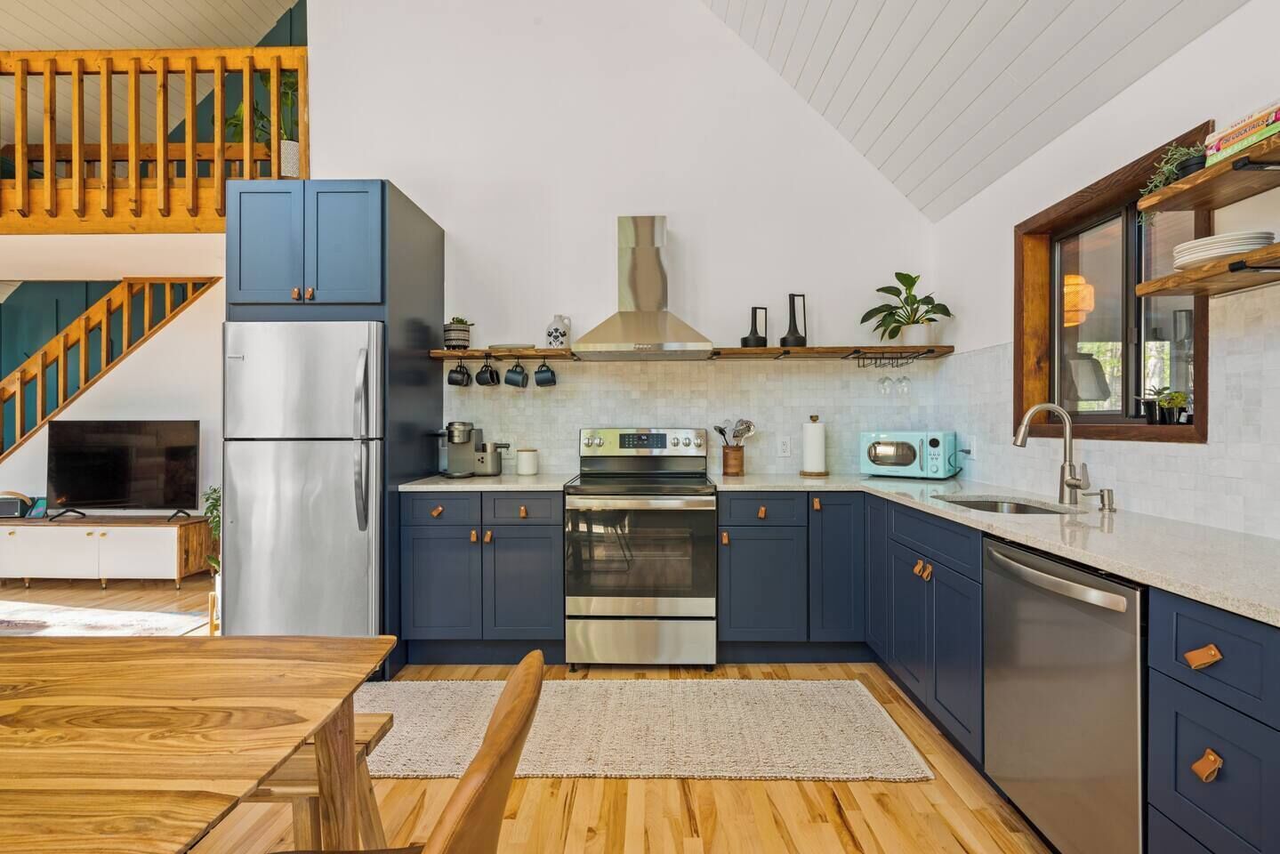 Una cucina moderna con mobili blu scuro, elettrodomestici in acciaio inossidabile e un tavolo da pranzo in legno.