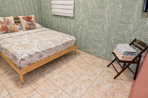 Un dormitorio con cama, una silla y ventana.