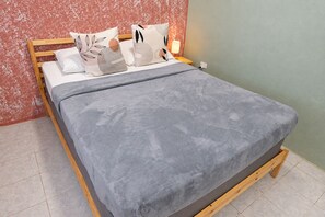Cama com cobertor cinza, cabeceira de madeira e várias almofadas com diferentes padrões.