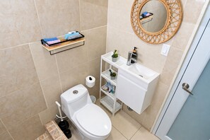 A bathroom with a toilet, sink, mirror, and shelves with toiletries. - Salo-Casa Verde 2nd floor by Stay Here PR (San Juan)