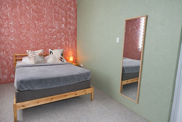 A bedroom with a bed, pillows, a nightstand, a mirror, and a wall with a textured pattern.