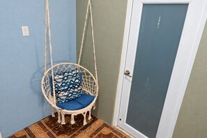 Habitación de esquina con una puerta blanca, pared azul y un sillón colgante con cojín estampado.