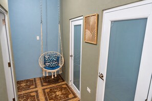 A hallway with a hanging chair, a door with a decorative panel, and patterned flooring.