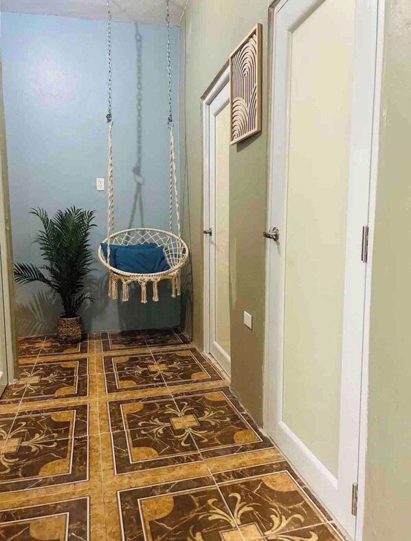 Stylish hallway with a geometric tile floor, a door, a hanging chair, and a potted plant.