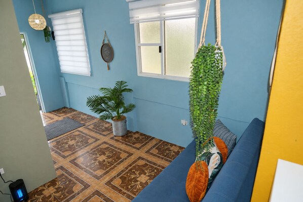 Una habitación con suelo estampado, un sofá azul, una planta colgante y un espejo montado en la pared.
