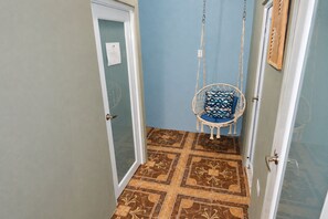 A narrow hallway with patterned floor tiles, a white door with a frosted glass panel, and a hanging chair with a cushion. - Salo-Casa Verde 2nd floor by Stay Here PR (San Juan)