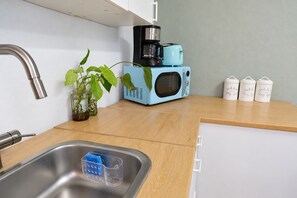 Cozinha equipada com pia, cafeteira, micro-ondas, uma planta e potes de armazenamento.