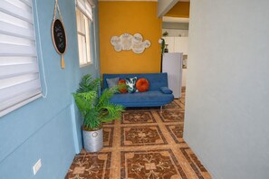 Un corridoio con un divano blu, piatti decorativi, una pianta in vaso e un pavimento a motivi.