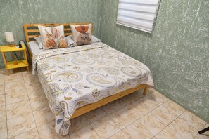 Una camera da letto con un letto in legno, una coperta a motivi decorativi, un comodino con una lampada e un condizionatore d'aria a parete.