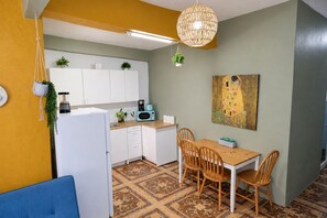 Cozinha compacta com armários brancos, micro-ondas, cafeteira e planta pendente.