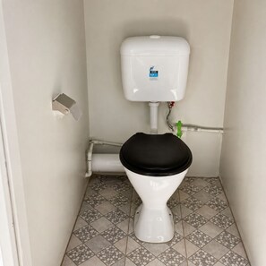 A toilet with a black seat and lid, a white tank, and a tiled floor with a geometric pattern. - Nananu-I-Ra Oceanfront House - Island Escape (Rakiraki)
