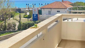 Un hôtel avec vue sur la mer et les montagnes. On peut voir un panneau indiquant l’emplacement du parking et une statue de grenouille sur le balcon.