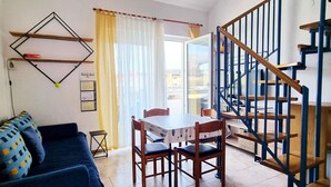 Un salon avec un canapé, une table à manger avec des chaises, un escalier et un calendrier accroché au mur.