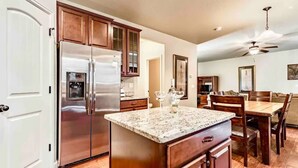 A kitchen with a stainless steel refrigerator, wooden cabinets, a granite countertop, and a dining area with a table and chairs. - The Haven @ Justice Wine~HotTub~Game Room (Colorado Springs)