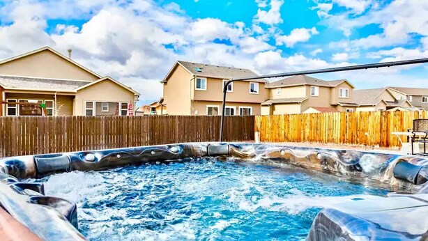 A hot tub in a backyard with a wooden fence and houses in the background. - The Haven @ Justice Wine~HotTub~Game Room (Colorado Springs)