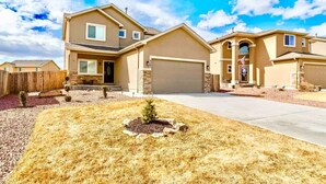 A two-story house with a garage, a front yard with a small tree, and a clear sky. - The Haven @ Justice Wine~HotTub~Game Room (Colorado Springs)