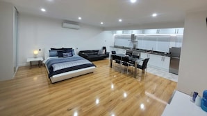 A modern bedroom with a bed, a small bedside table, a black sofa, and a kitchenette area with cabinets and a stove. - Resort Style Apartment Escape with Heated Pool, Tennis Court Outdoor BBQ (Bellevue Heights)