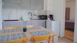 A compact kitchen with grey cabinets, a microwave, a coffee maker, and a small fridge. There is a dining table with two chairs and a potted plant. - Holiday apartment Apartment for 3 people with garden views (Starigrad-Paklenica)