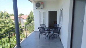 A balcony with a table and chairs, an air conditioning unit, and a view of greenery and buildings. - Holiday apartment Apartment for 3 people with garden views (Starigrad-Paklenica)