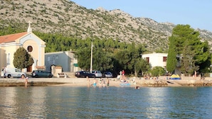 A coastal scene with a church, parked cars, and people by the water. - Holiday apartment Apartment for 3 people with garden views (Starigrad-Paklenica)