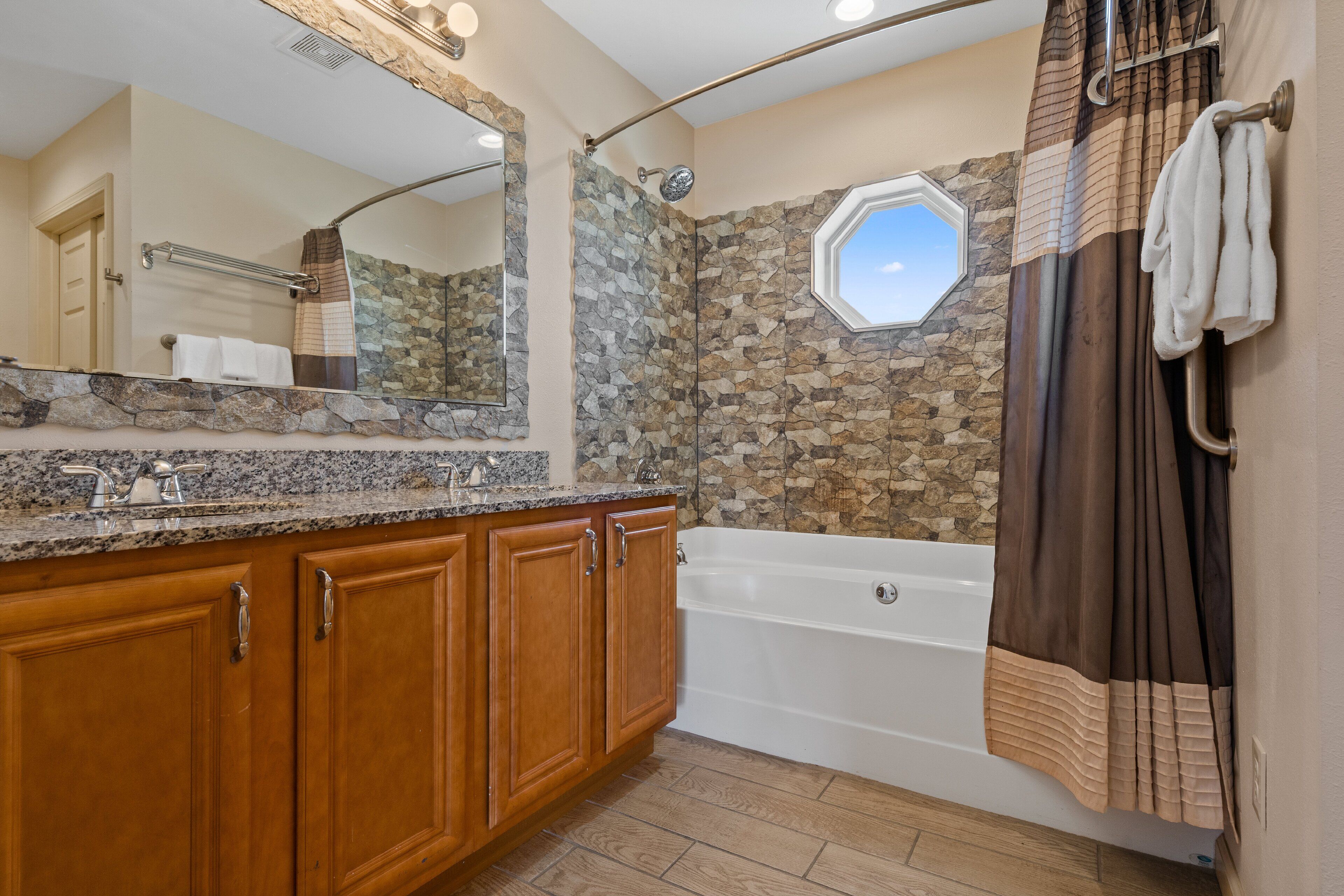 Un baño con pared de piedra, bañera, armarios de madera y un espejo grande.