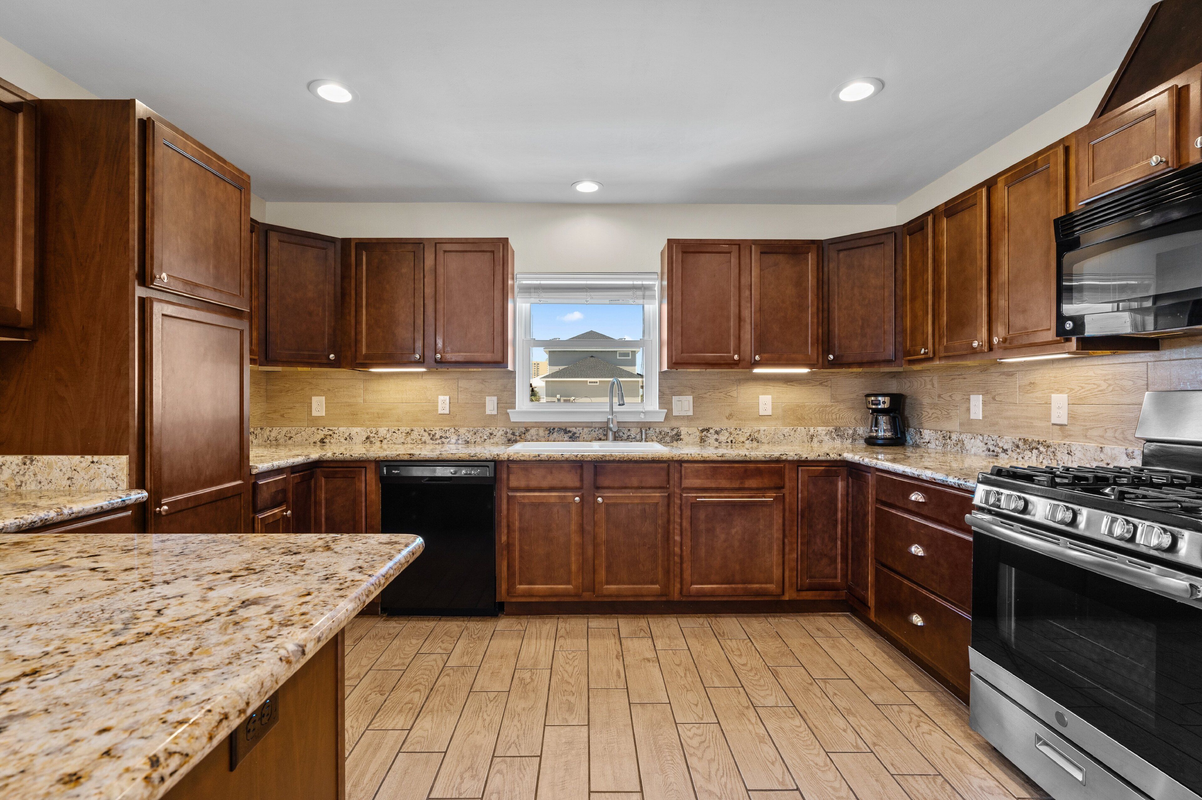 A kitchen with wooden cabinets, granite countertops, a dishwasher, a stove, and a window with a view.
