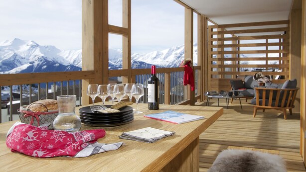 A wooden deck with a table set for dining, overlooking a snowy mountain range. - Magnifique vue sur les pistes, exposé sud, garage (Alpe d'Huez)