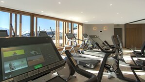 A modern gym with treadmills, exercise bikes, and a large screen displaying workout routines. - T3 + Vue sur les pistes | Emplacement privilégié (Alpe d'Huez)