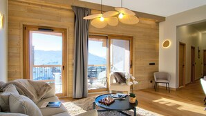 A spacious living room with a large window, a cozy sofa, a small table with a chessboard, and a chair. - T3 + Vue sur les pistes | Emplacement privilégié (Alpe d'Huez)