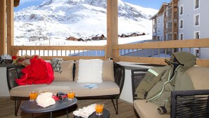 A balcony with a view of snow-covered mountains, a sofa, a table with drinks, and a jacket on the floor.