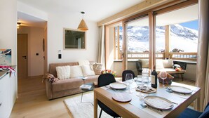A dining area with a table set for four, a sofa, and a view of snow-covered mountains through large windows.