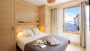A bedroom with a bed, pillows, a bedside lamp, a window with curtains, and a view of a snowy mountain.